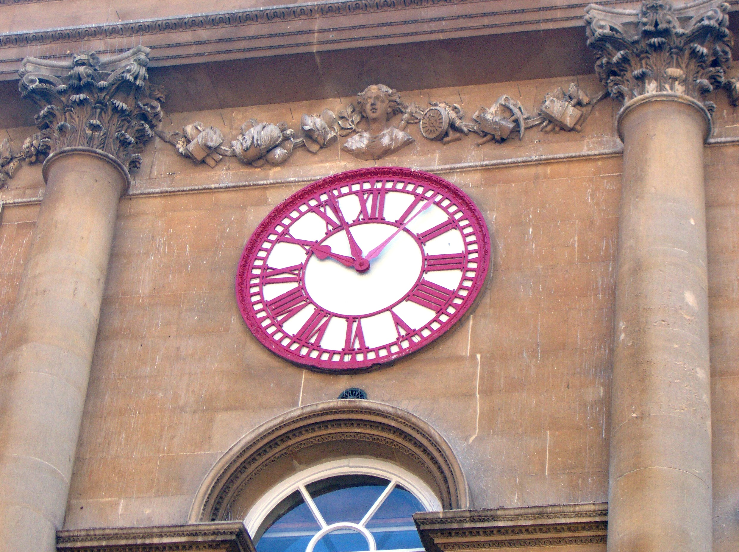 A 19th century clock on the outside of a railway station. The clock has two minute hands, one eleven minutes behind the other.